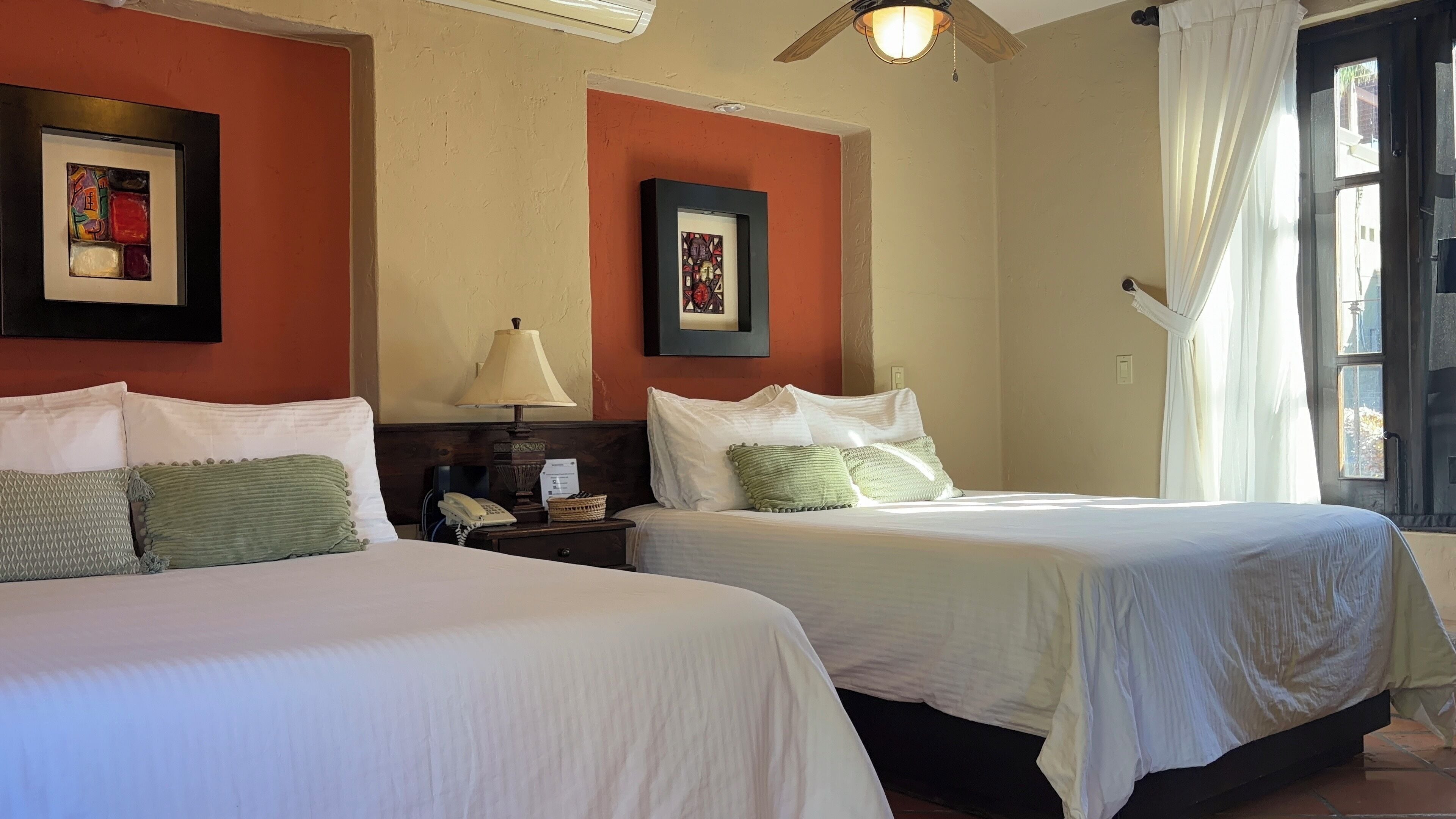 A hotel room with two beds, a nightstand with a lamp, and artwork on the walls.