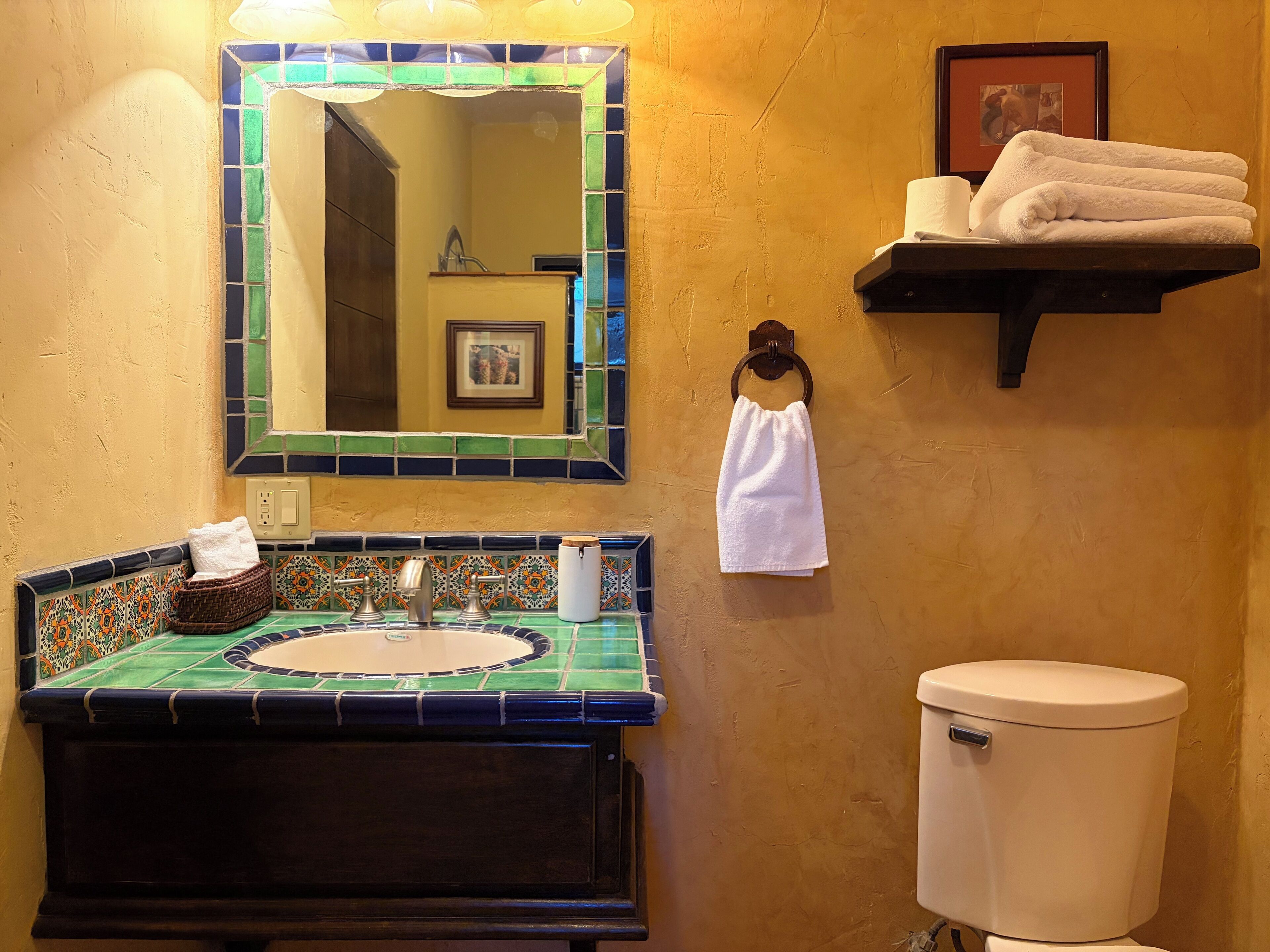 A bathroom with a tiled sink, a mirror, a towel rack, and a toilet.