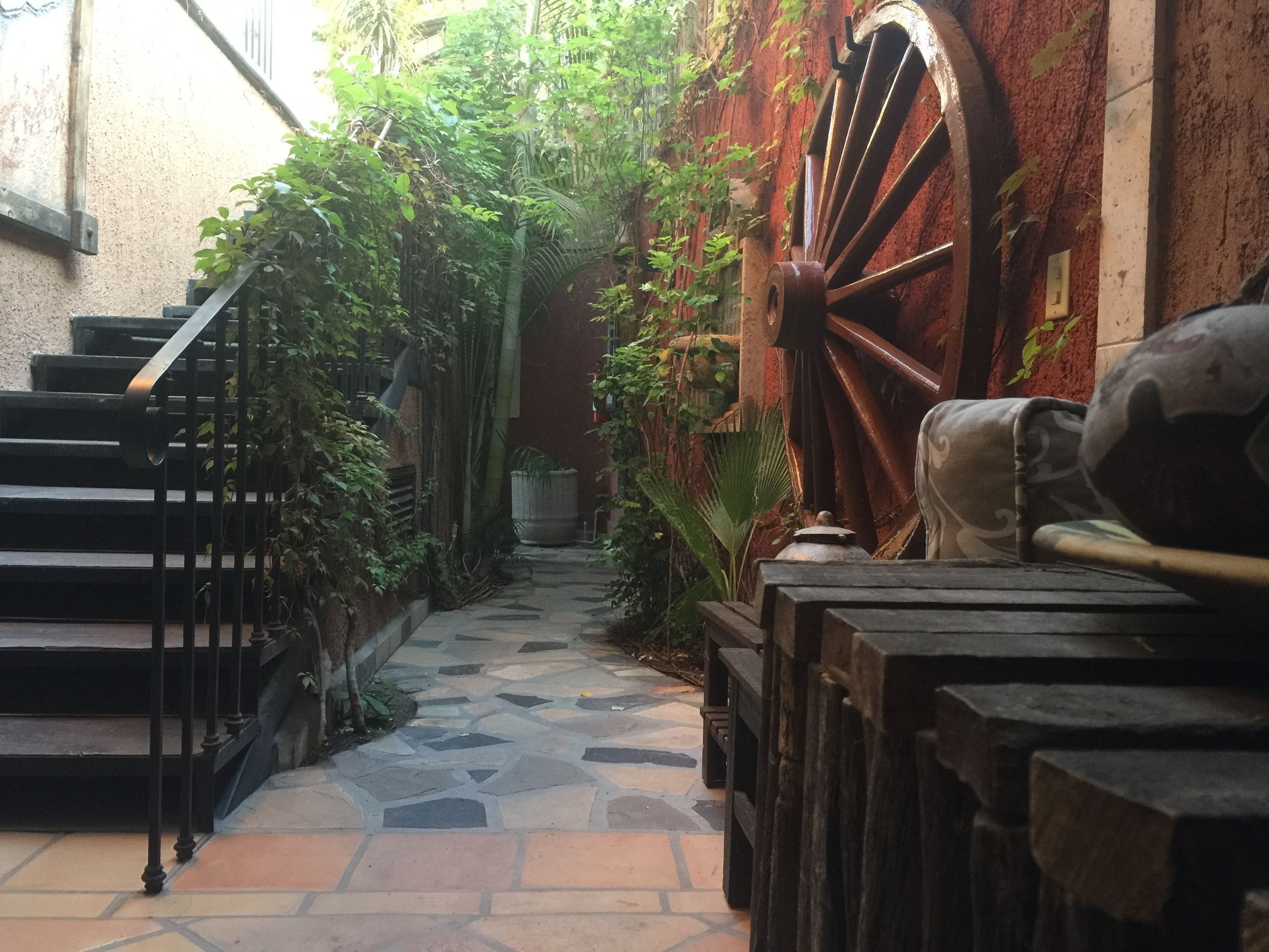 A narrow stone pathway leading to a staircase with a large wooden wheel structure on the right.