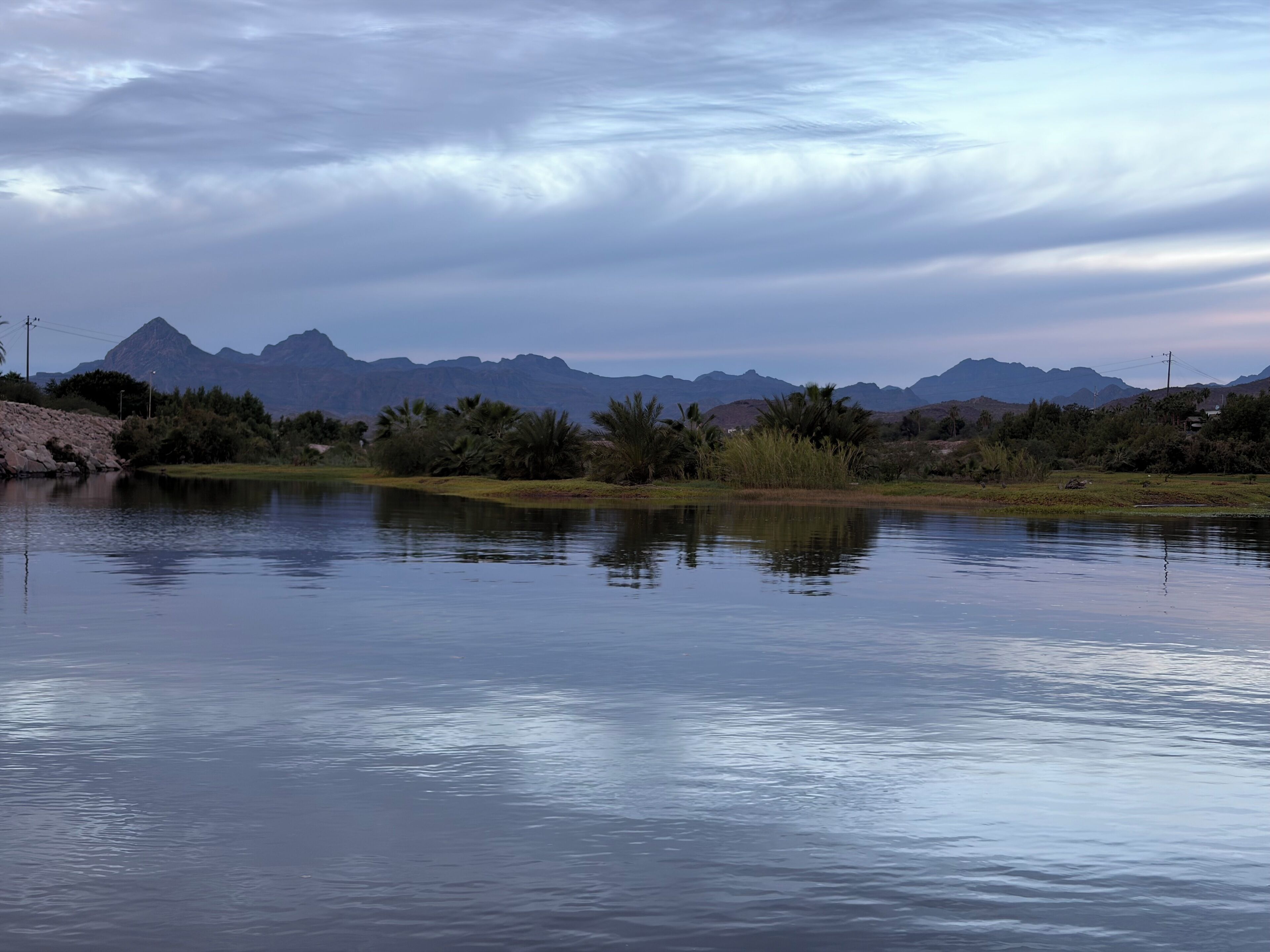 A calm lake with mountains in the background and some vegetation around.