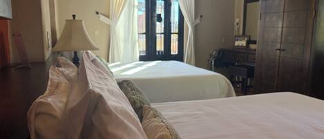A hotel room with two beds, a wooden wardrobe, a desk, and a window with curtains.