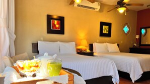 Une chambre d'hôtel avec deux lits, une table de chevet en bois sur laquelle se trouve un plateau de petit-déjeuner, un ventilateur de plafond et des œuvres d'art accrochées aux murs.