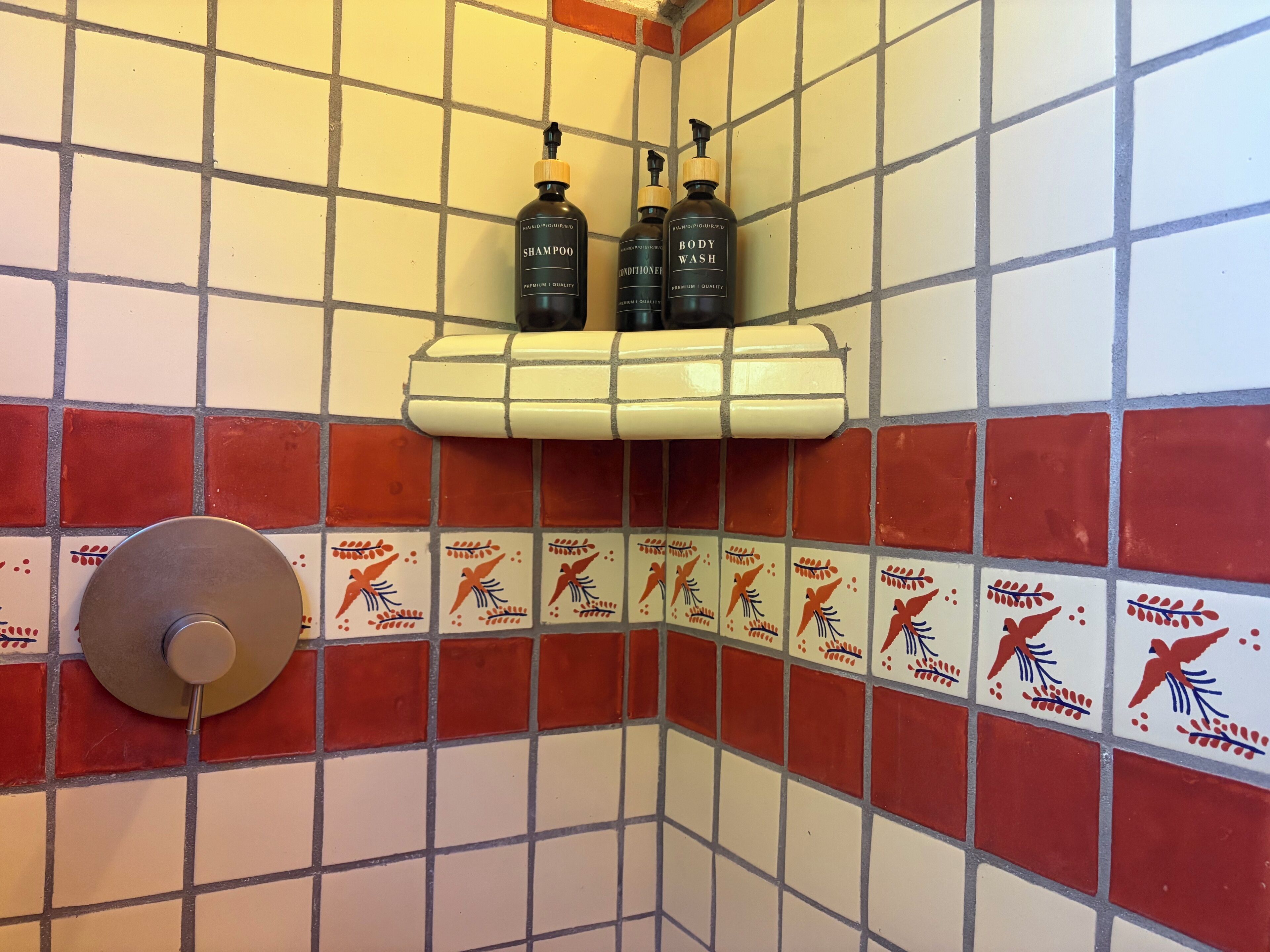 Ein Badezimmer mit Fliesenwänden, einer Duschbrause und zwei Flaschen Shampoo und Badeschaum auf einem Regal.