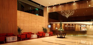 A modern hotel lobby with red seating, a reception desk, and a large decorative light fixture.