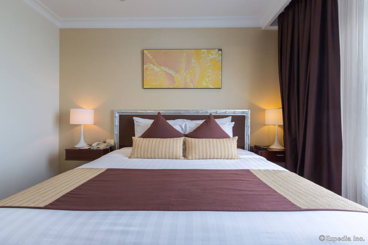 Habitación de hotel con una cama grande, dos lámparas de noche, una mesita con teléfono y un cuadro en la pared.