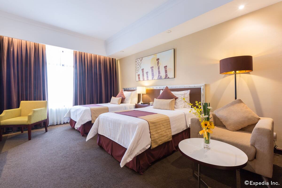 Habitación de hotel con dos camas, un sofá, una silla, una lámpara y un florero con flores.
