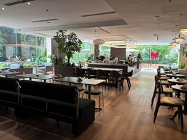 A modern cafe with wooden tables and chairs, a bar area, and large windows offering a view of greenery.