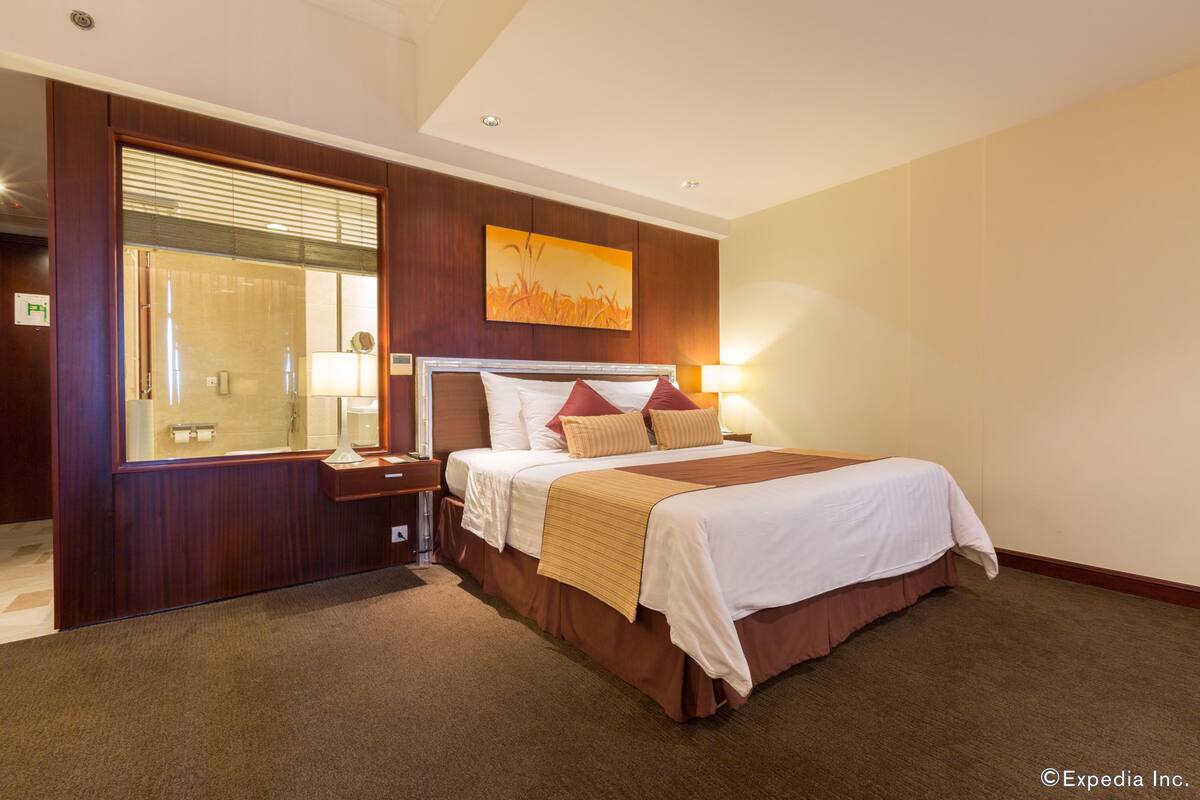 Una habitación de hotel con una cama grande, una mesita de noche, un espejo y una ventana con persianas.