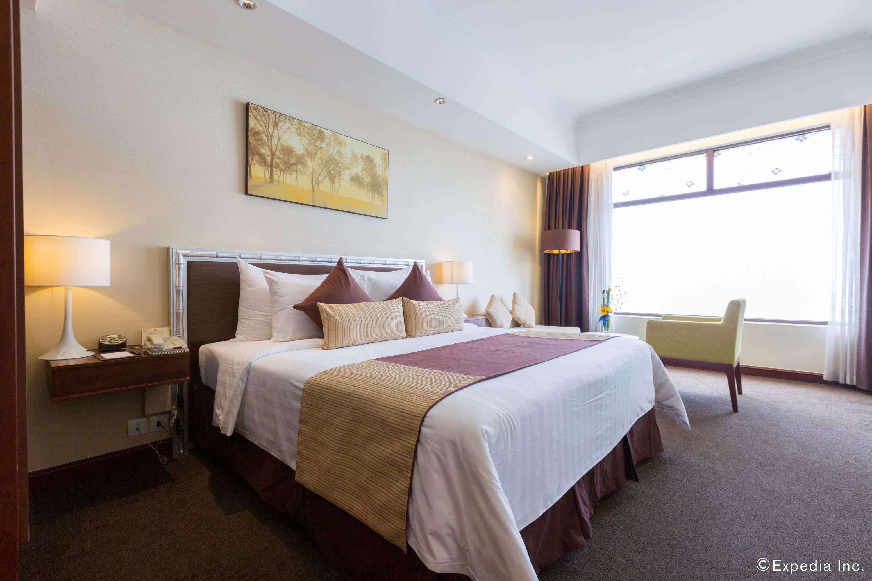 A hotel room with a large bed, bedside lamps, a desk with a telephone, and a window with curtains.