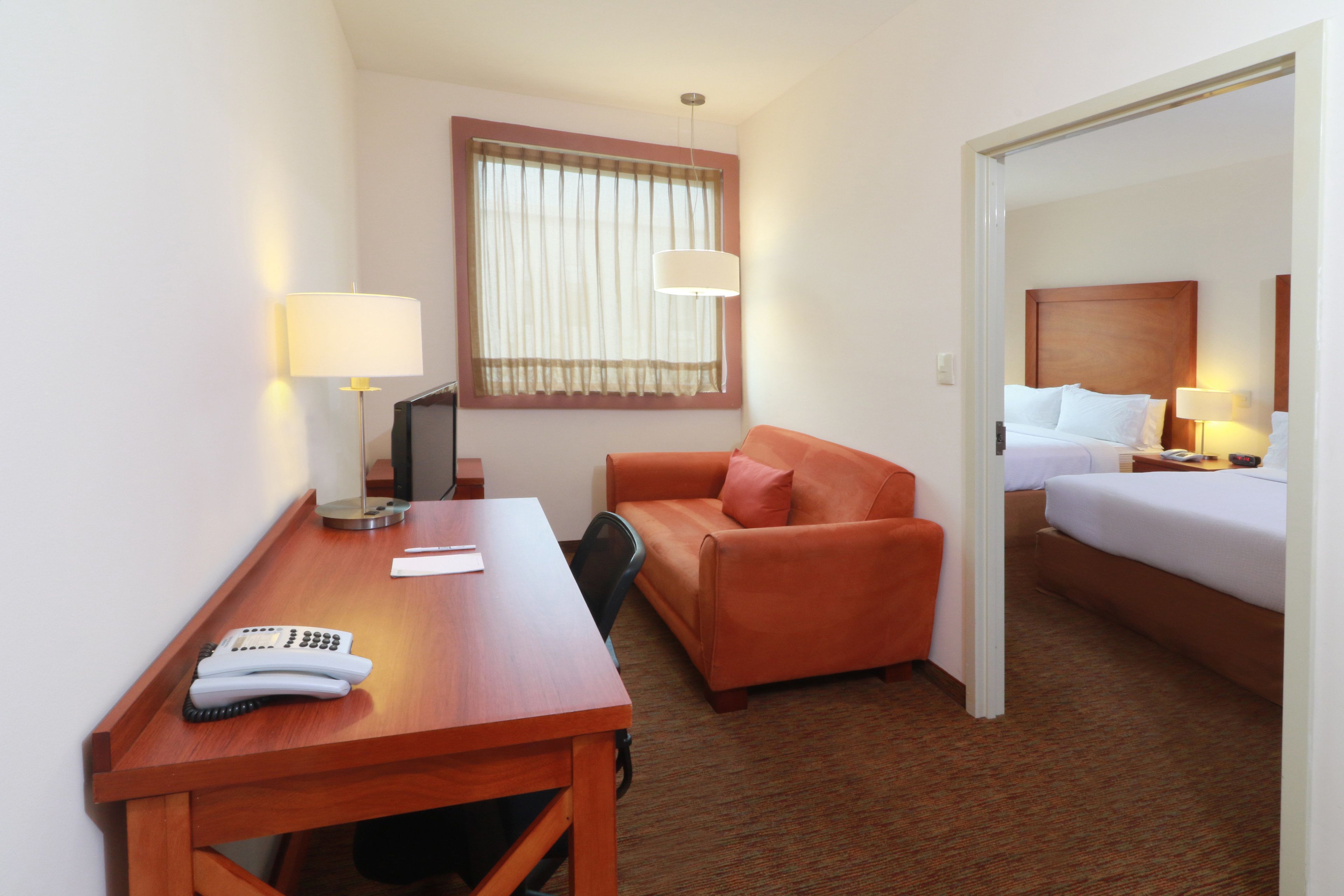 A hotel room with a wooden desk, a sofa, a bed, and a window with curtains.