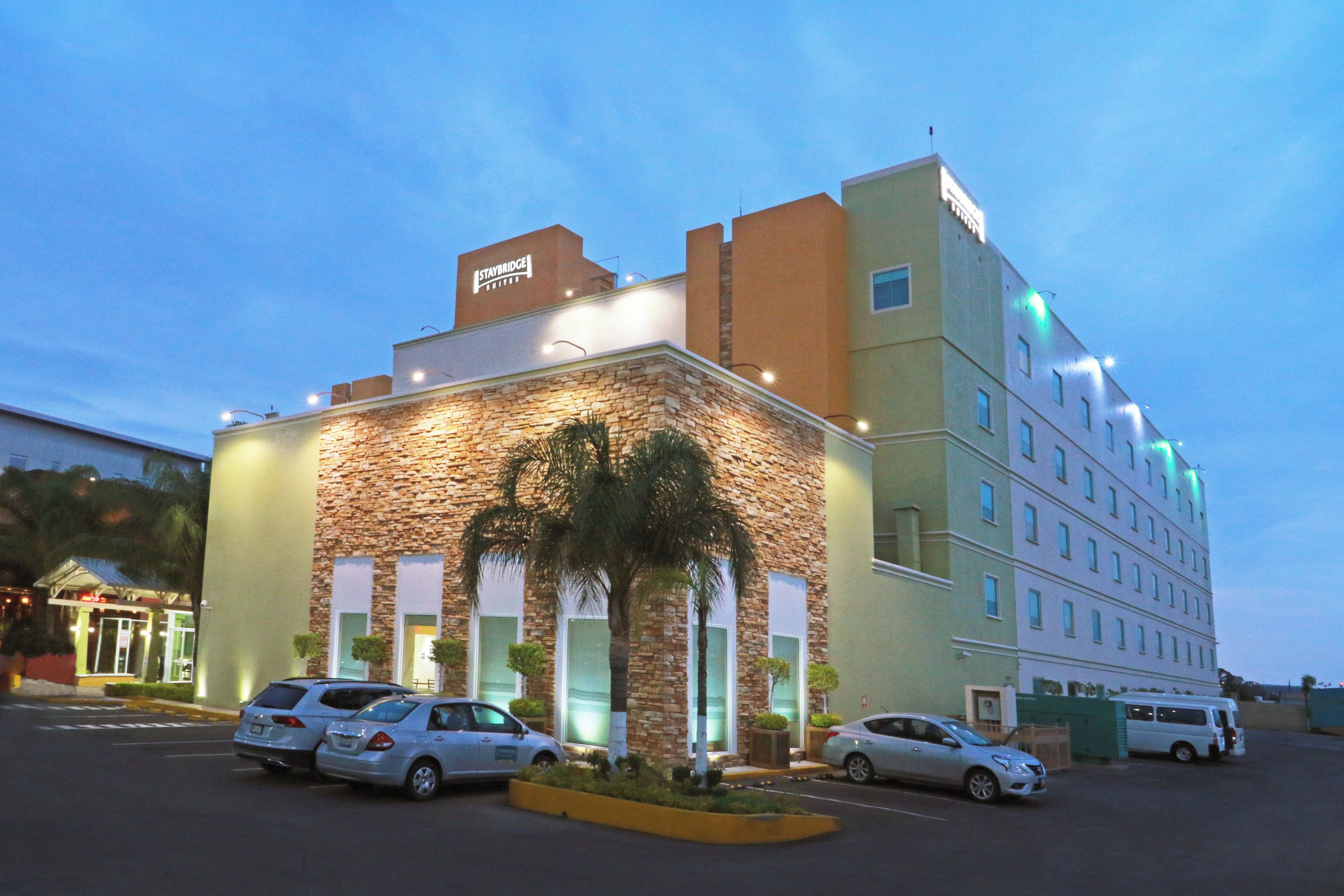 Un hotel de fachada de piedra, varios pisos y un estacionamiento con varios autos.