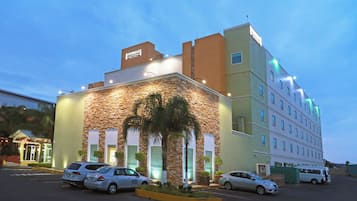 Un hotel de fachada de piedra, varios pisos y un estacionamiento con varios autos.