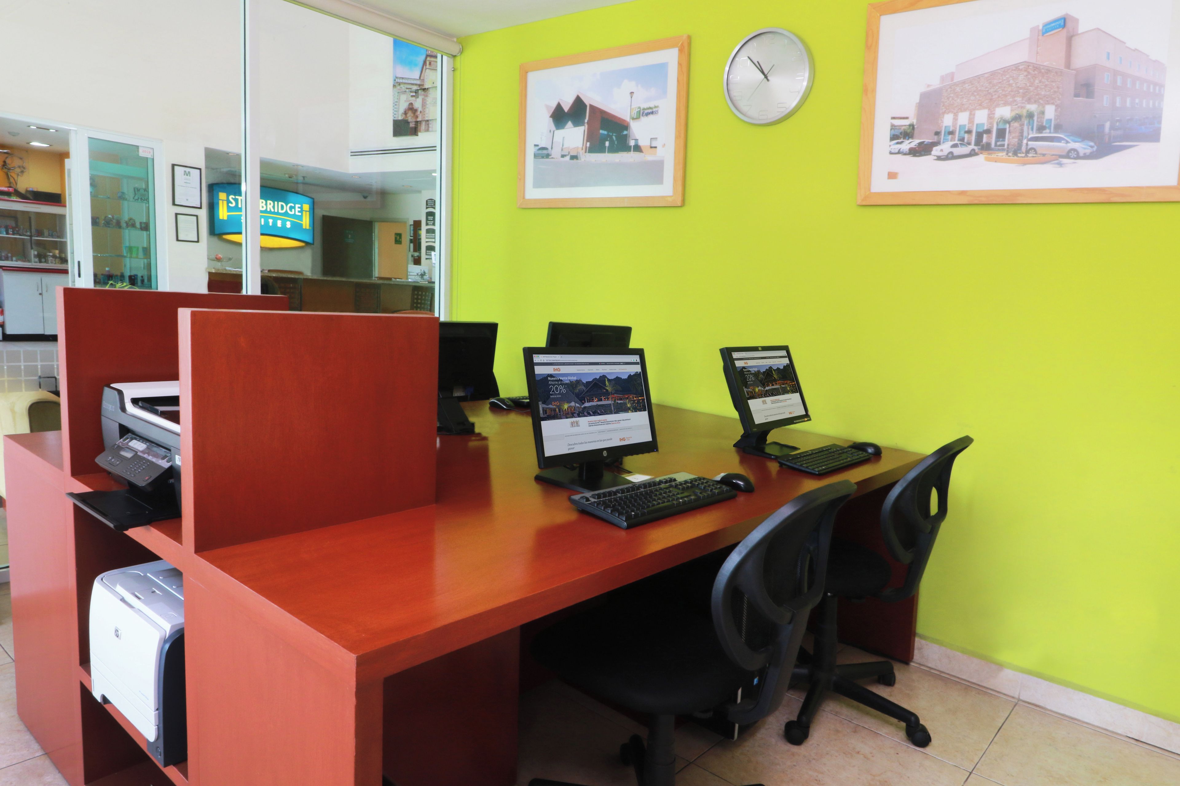 Un bureau d’hôtel avec des cloisons, des ordinateurs et une horloge au mur.