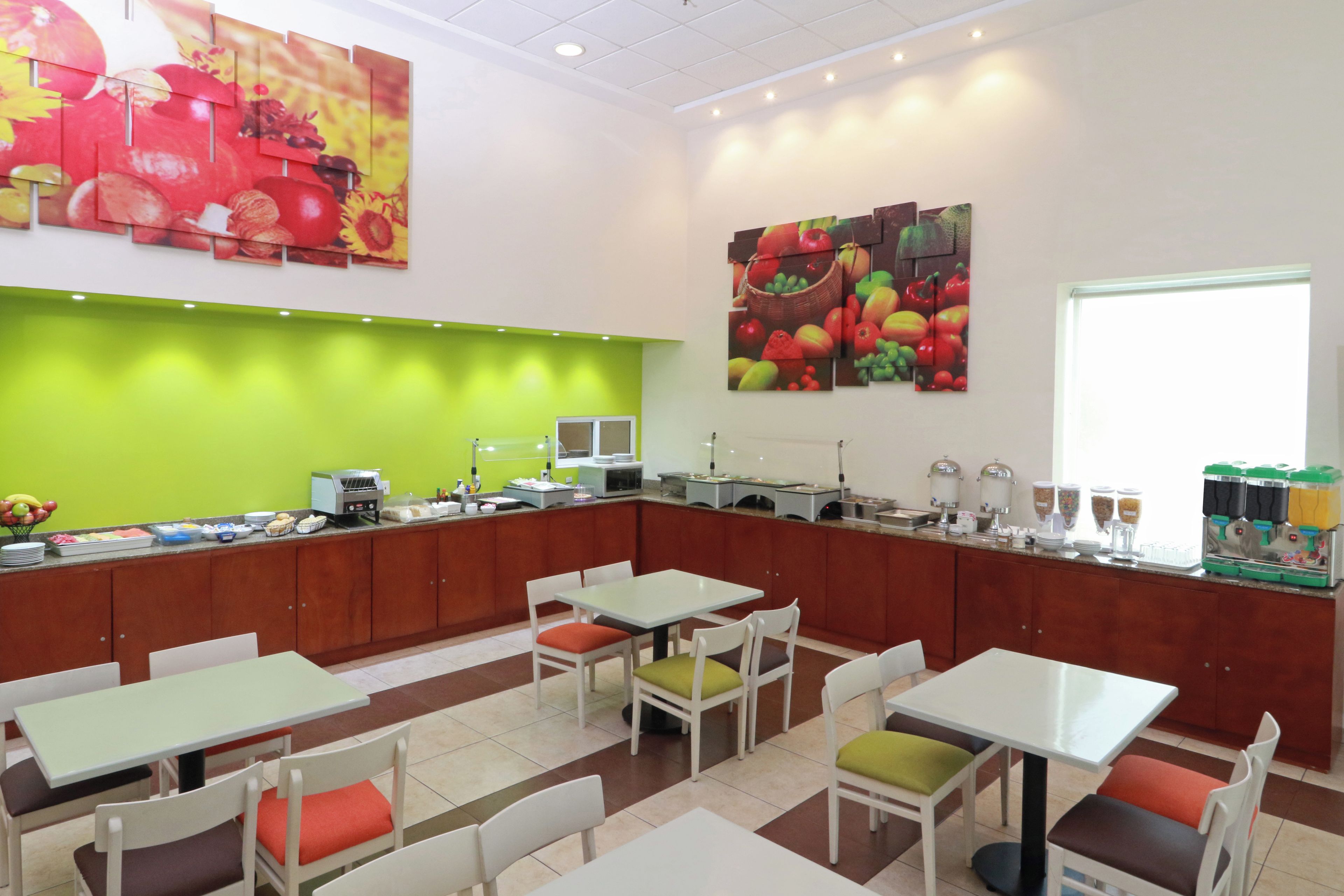 A cafeteria with tables and chairs, a food service area with a microwave, and a large fruit-themed wall mural.