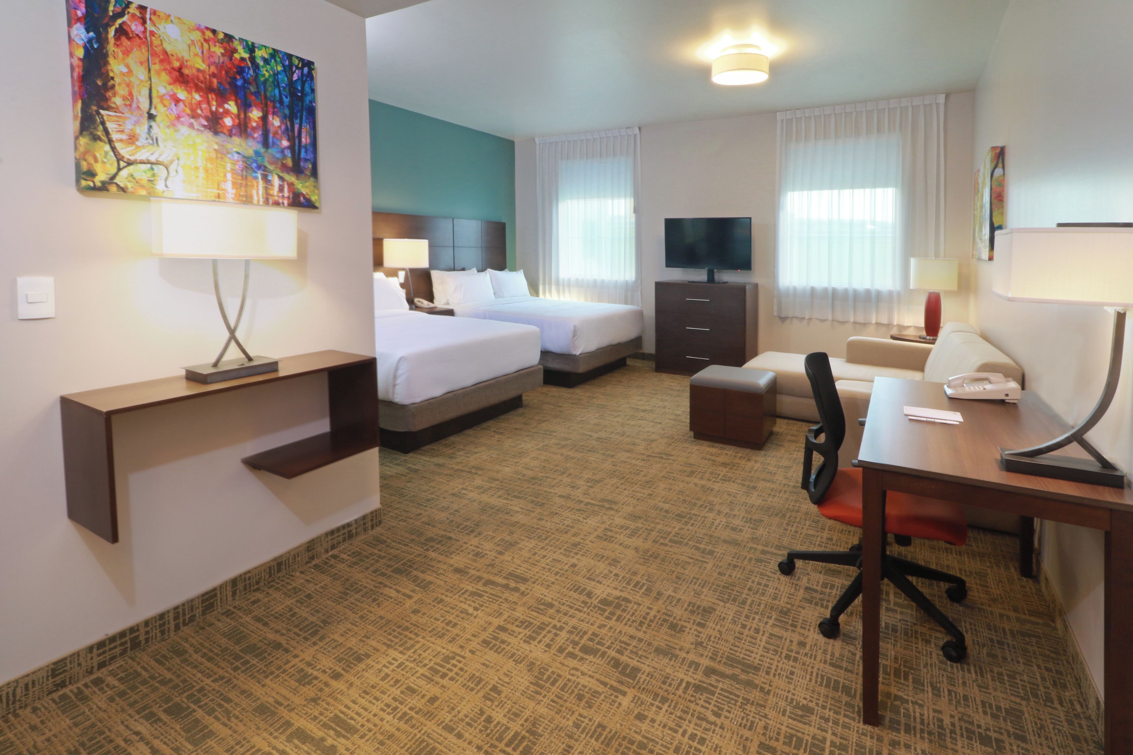 A hotel room with two beds, a desk, a television, and a painting on the wall.