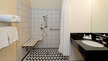A bathroom with a checkered floor, a shower with a handheld showerhead, a sink, and a towel rack.