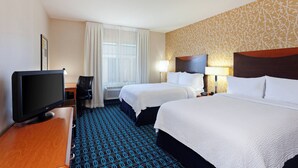 Habitación de hotel con dos camas, televisión, escritorio y alfombra estampada.