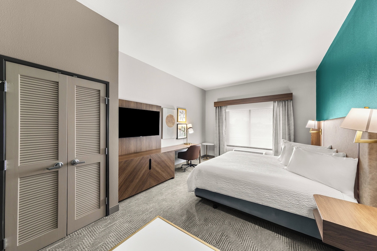 A hotel room with a large bed, a desk, a TV, and a wardrobe.