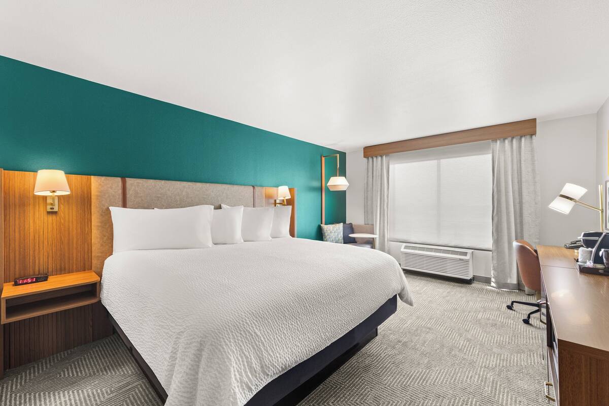 Ein Hotelzimmer mit einem großen Bett, Nachttischen mit Lampen, einem Schreibtisch mit Stuhl und einem Fenster mit Vorhängen.