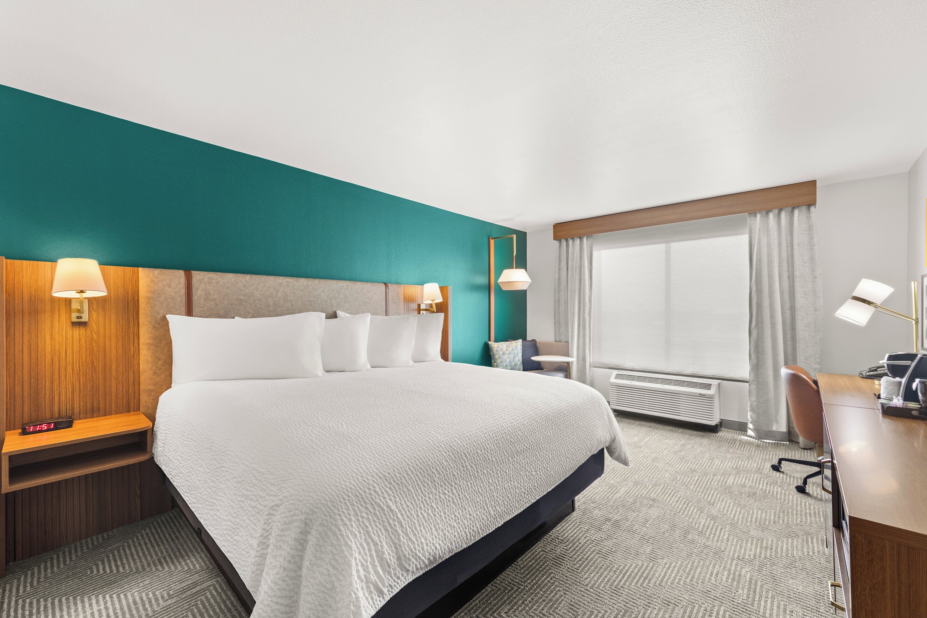 A hotel room with a large bed, bedside tables with lamps, a desk with a chair, and a window with curtains.