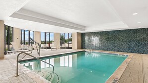 Piscina interior com água cristalina, um deck revestido de azulejos e uma parede com padrão em espinha de peixe.