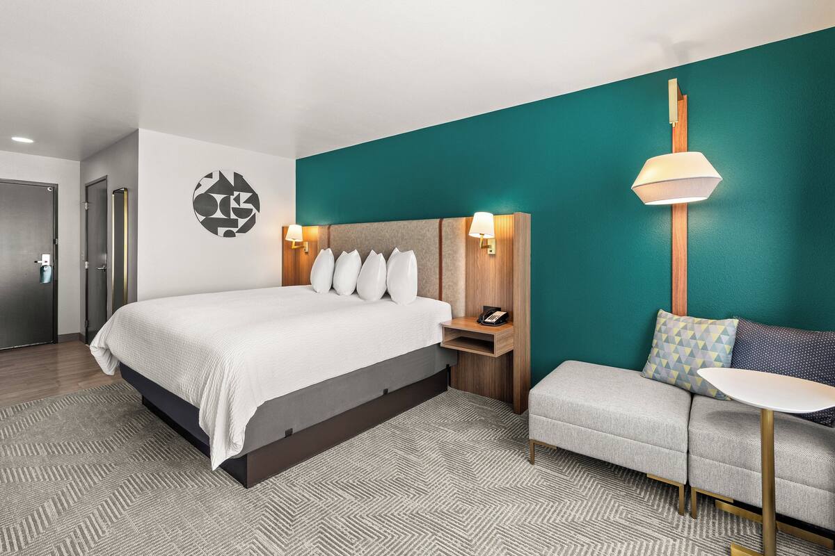 Ein modernes Hotelzimmer mit einem großen Bett, einer Sitzecke, einem kleinen Tisch und einer Wandlampe.