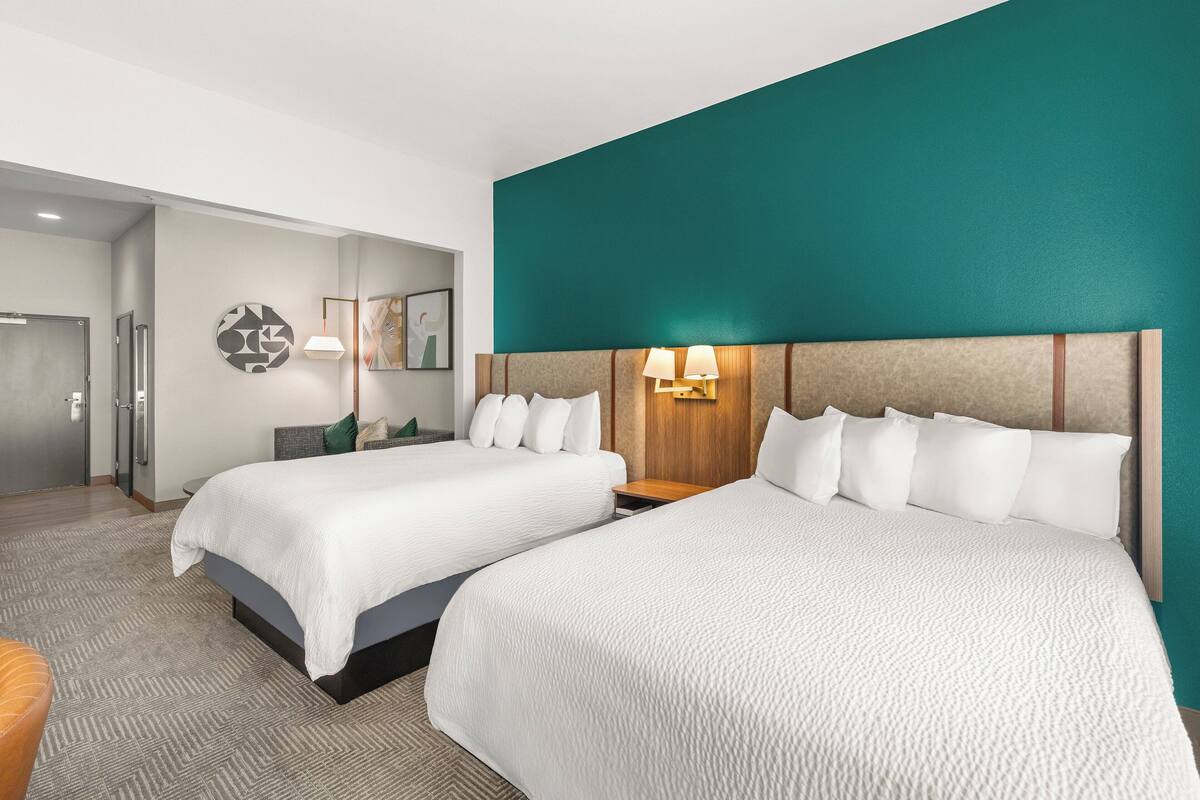 Ein Hotelzimmer mit zwei Betten, einem hölzernen Kopfteil, einer Wandlampe und einer Tür zu einem Badezimmer.