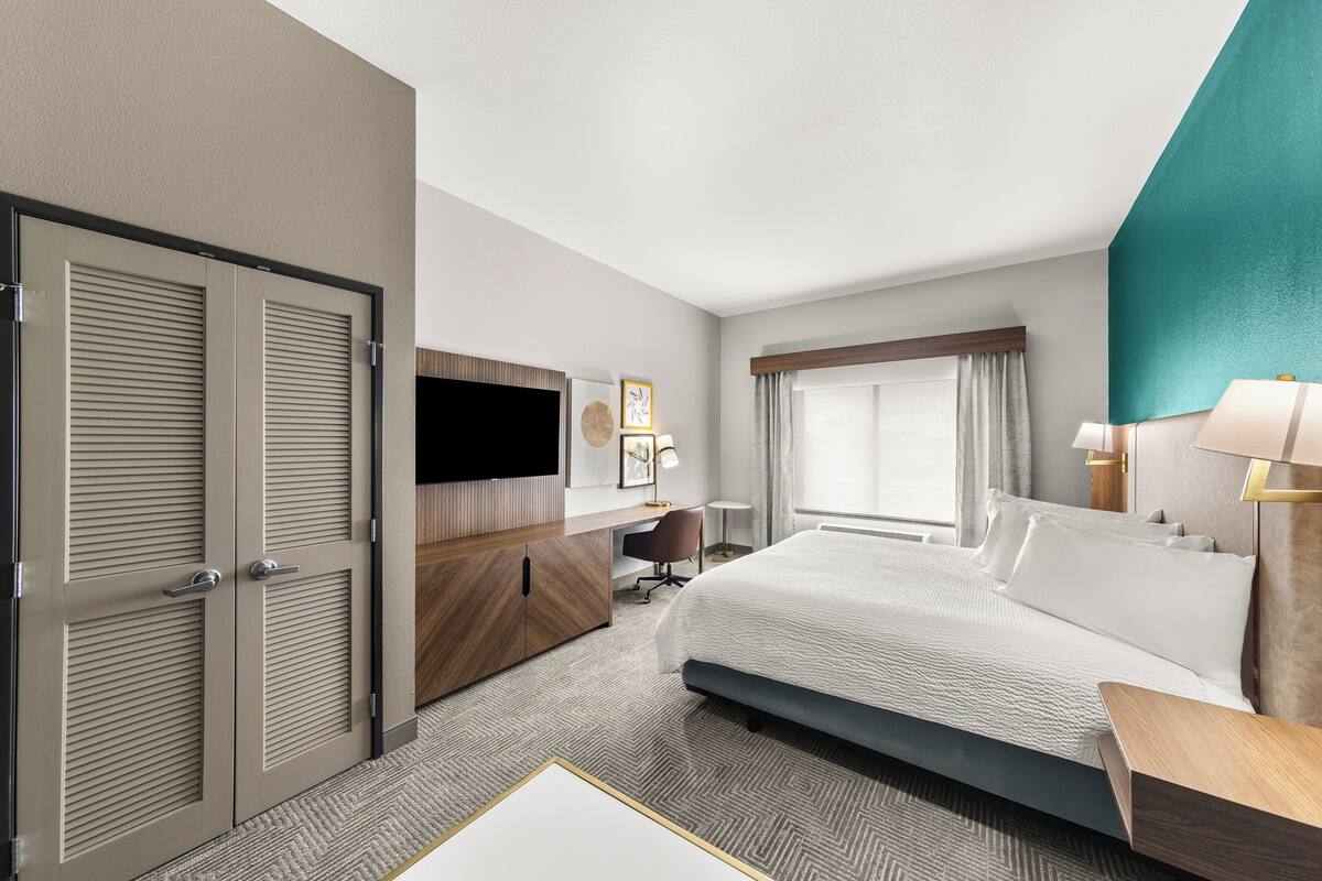 Ein Hotelzimmer mit einem großen Bett, einem Schreibtisch, einem Fernseher und einem Kleiderschrank.