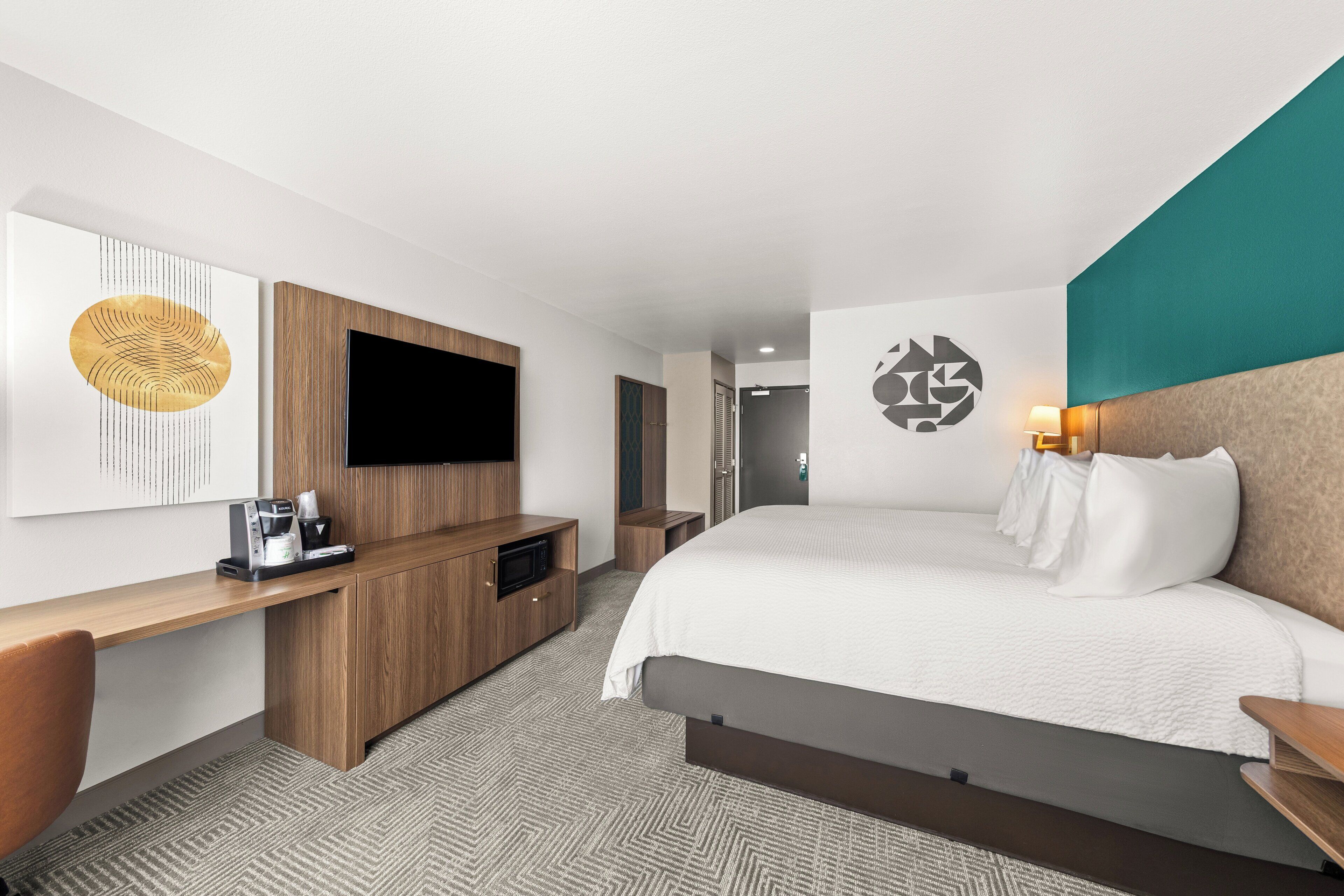 A hotel room with a bed, a TV, a desk, and a coffee machine.