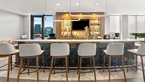 Uma área de bar moderna com bancada de mármore, banquetas e diversas garrafas.