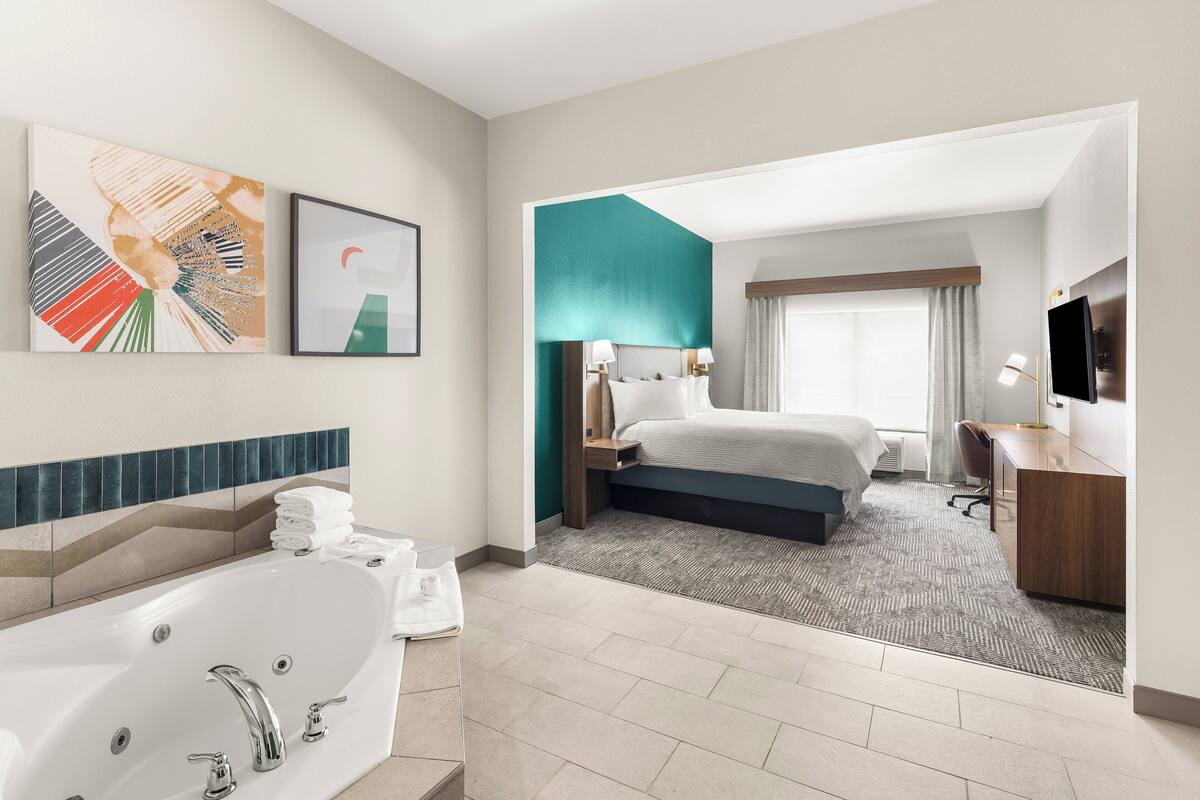 Ein modernes Hotelzimmer mit einer großen Badewanne, einem ordentlich bezogenen Bett, einem Schreibtisch mit Stuhl und einem Fernseher.