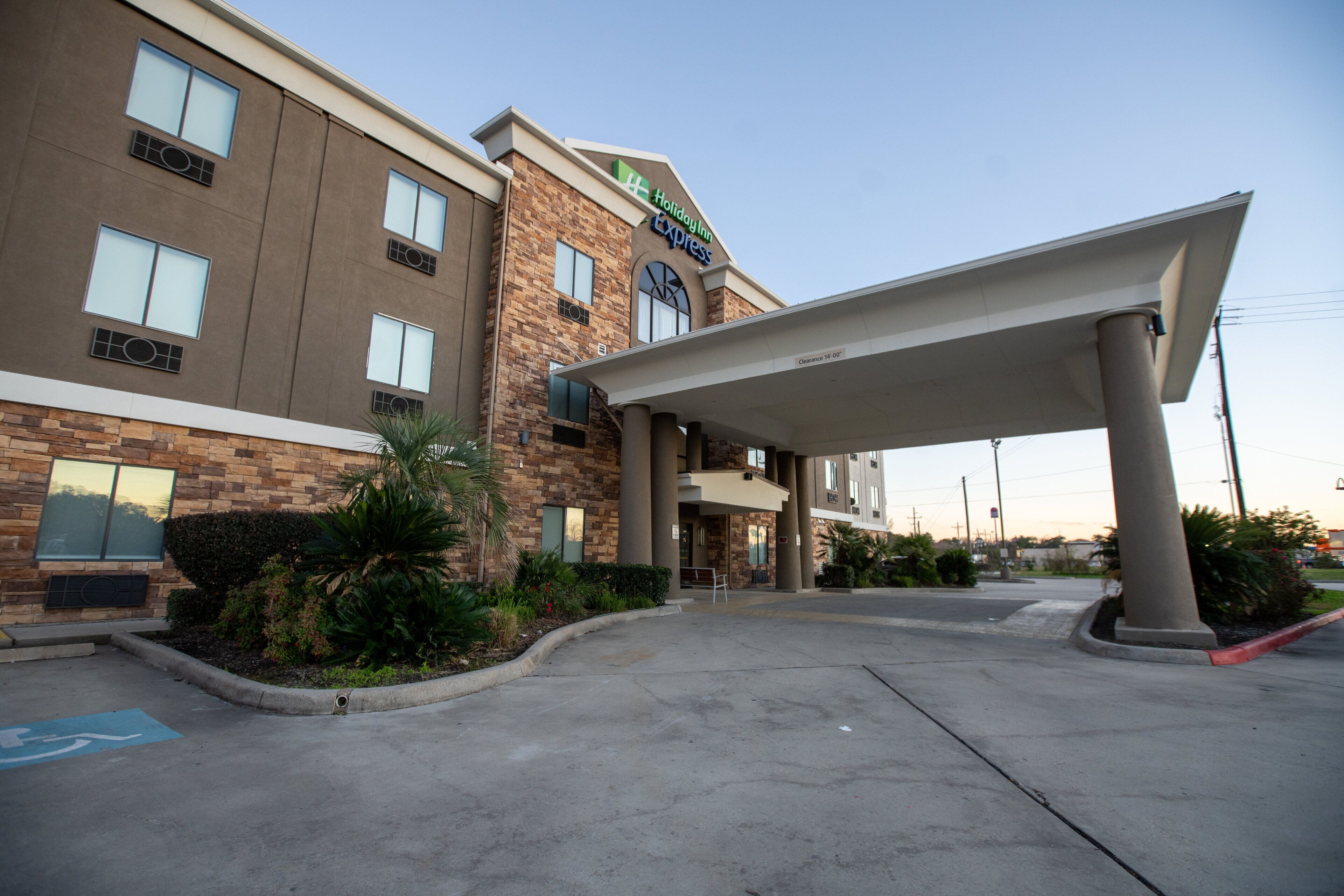 Edificio de Holiday Inn Express con entrada cubierta, estacionamiento y área ajardinada con plantas.