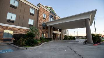 Edificio de Holiday Inn Express con entrada cubierta, estacionamiento y área ajardinada con plantas.