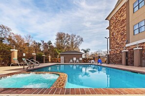 A swimming pool with a brick edge, surrounded by lounge chairs and a small building, likely a changing room or storage.