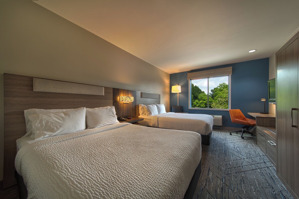Een hotelkamer met twee bedden, een bureau, een stoel, een raam met uitzicht en een wandlamp.