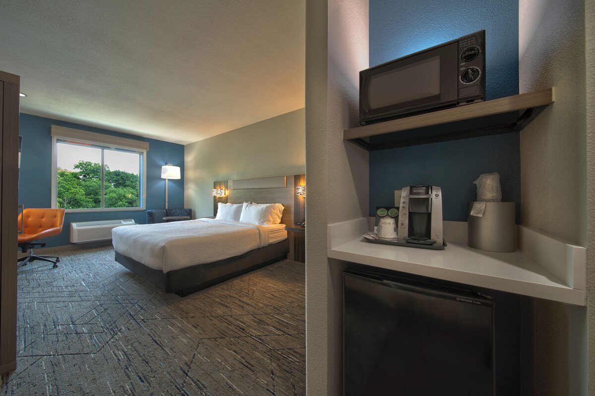 Een hotelkamer met een bed, een bureau, een stoel, een magnetron, een koffiezetapparaat en een koelkast.