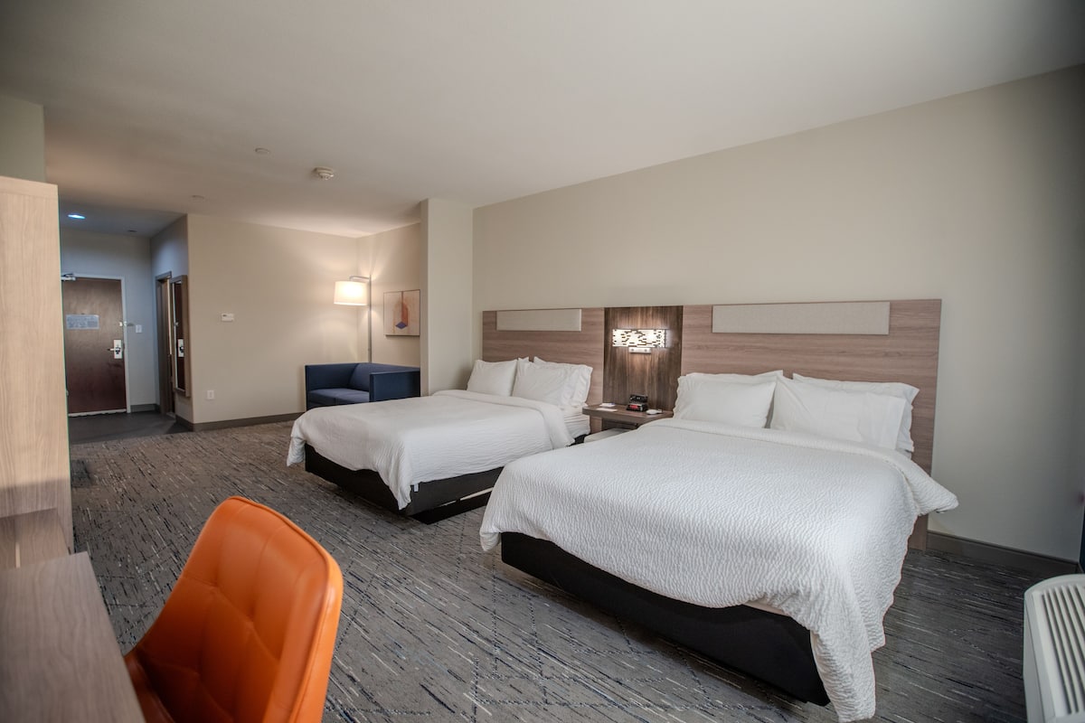A hotel room with two beds, a desk, and a chair.