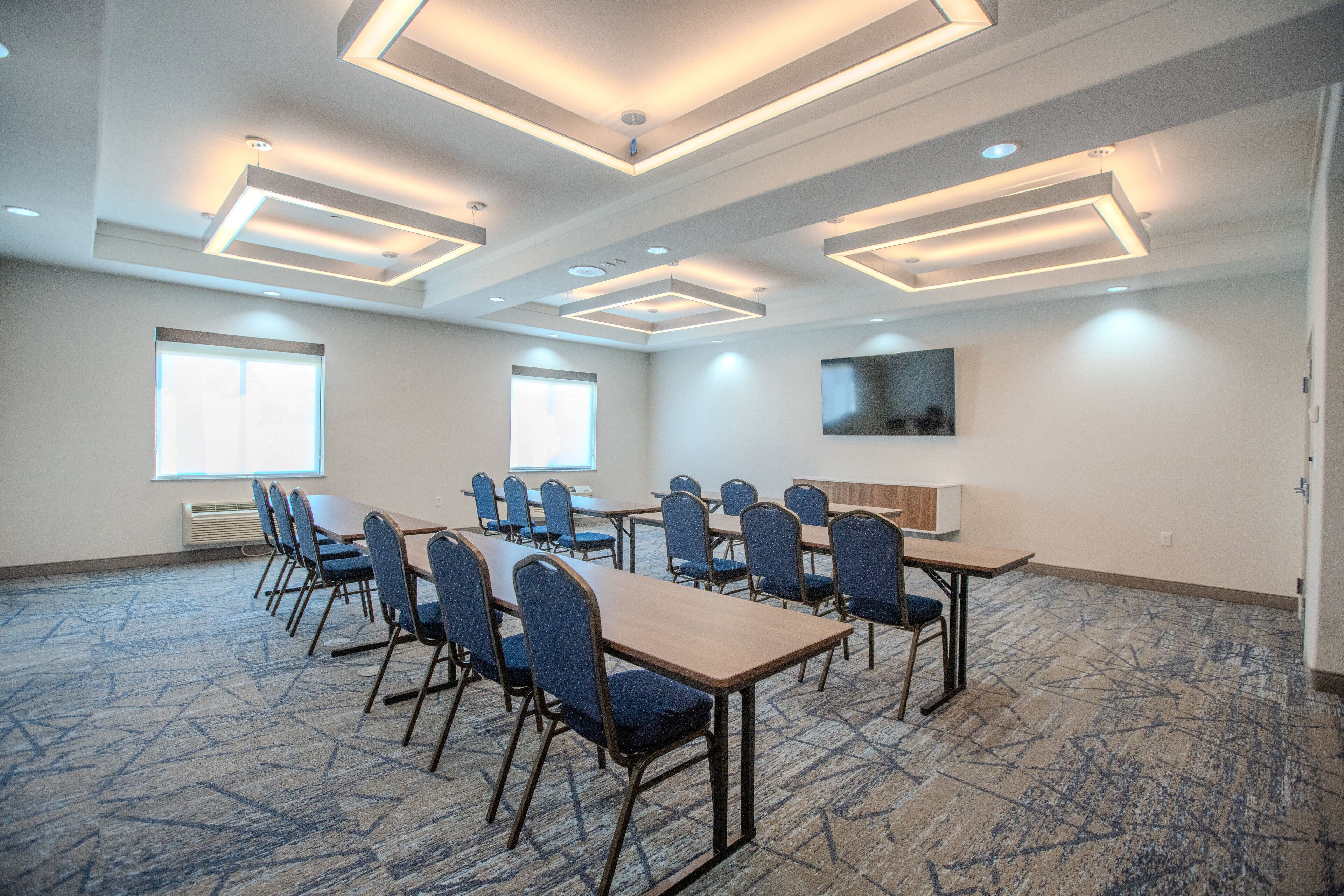 Un salón de conferencias con una mesa larga y sillas, un televisor de pantalla plana en la pared y una alfombra estampada.