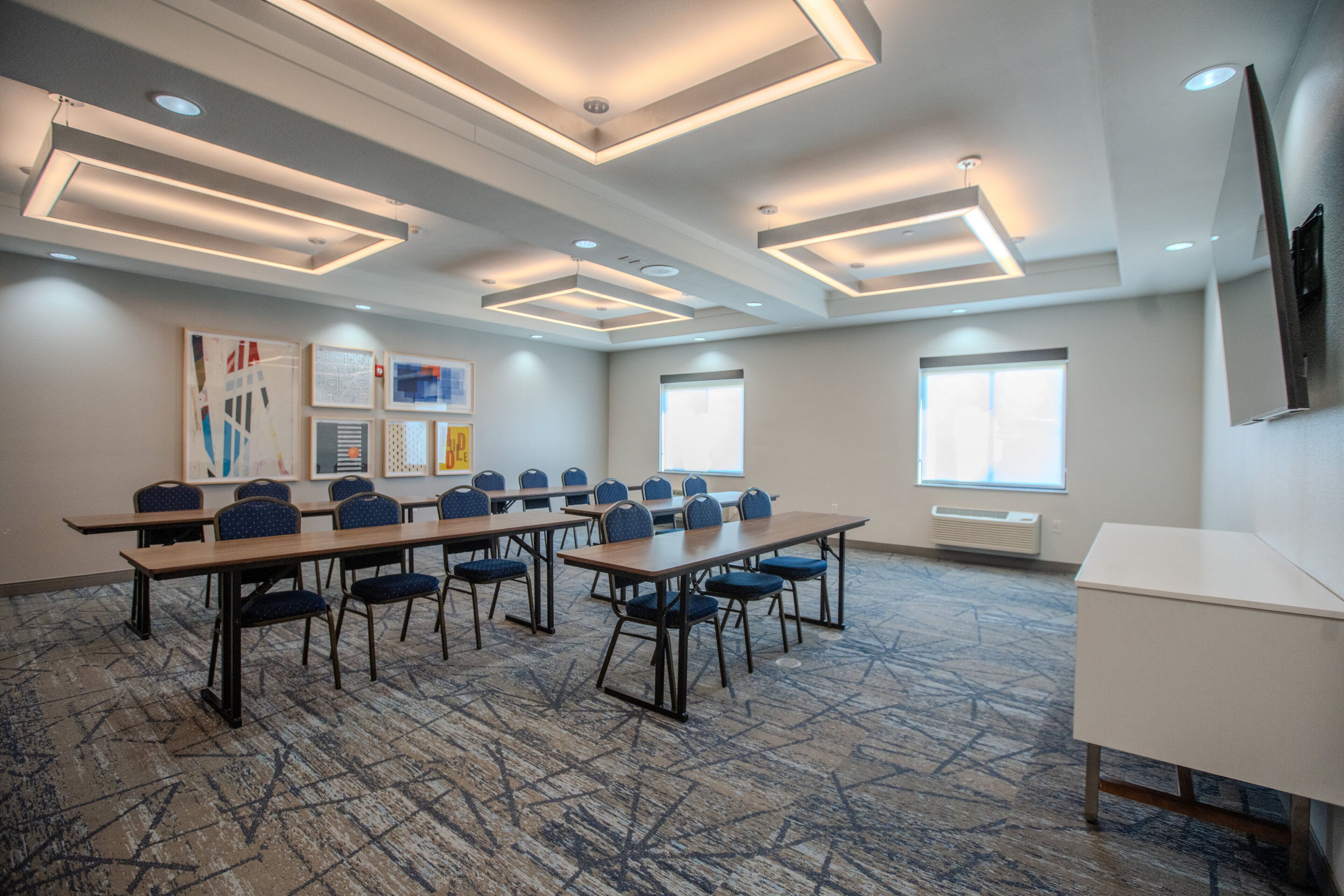 A conference room with tables and chairs, a carpeted floor, and ceiling lights.