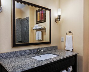 A bathroom with a granite countertop sink, a mirror with a black frame, and a towel rack with white towels.