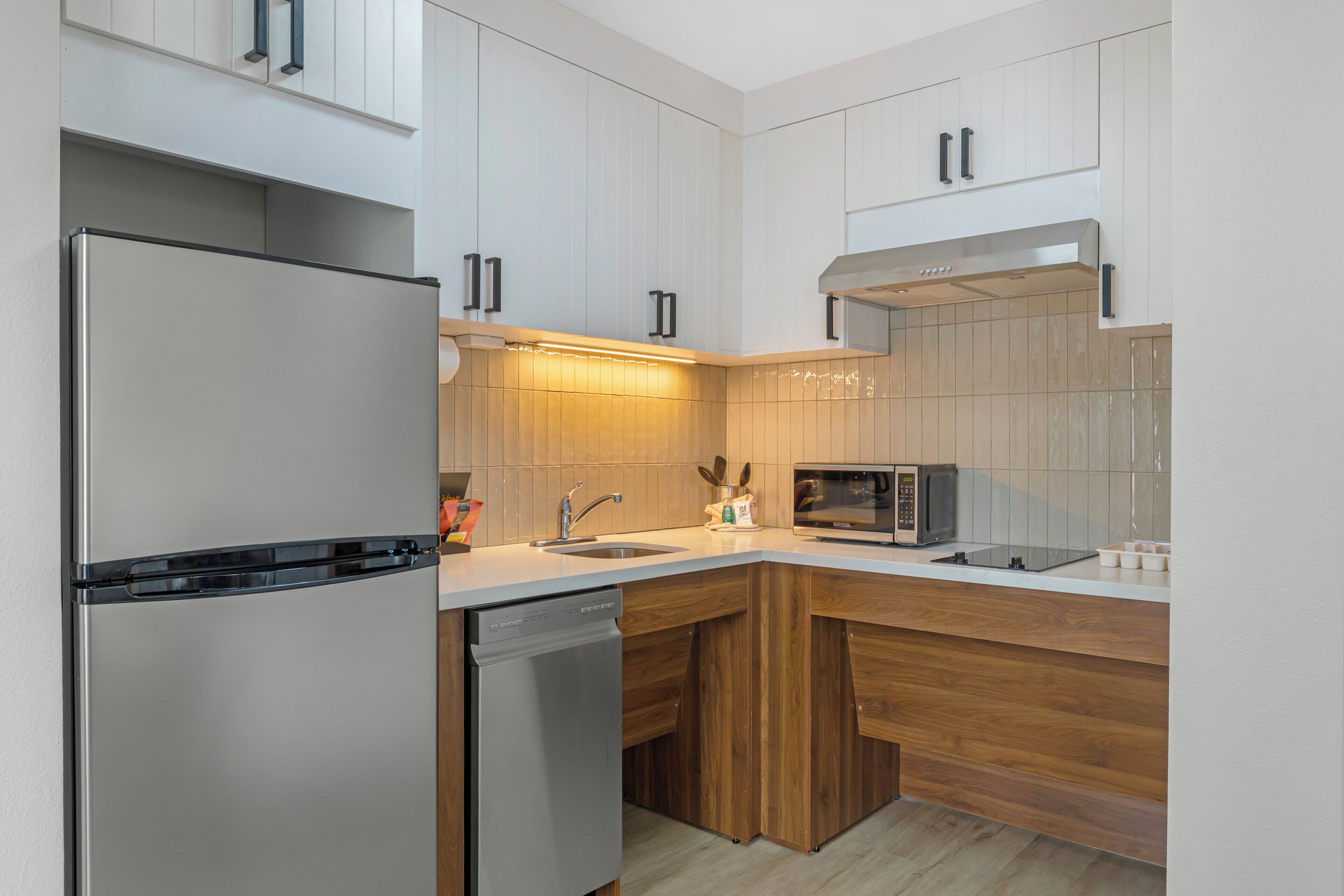 A modern kitchen with a stainless steel refrigerator, dishwasher, microwave, and wooden cabinets.
