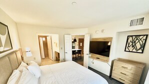 A hotel room with a large bed, a TV mounted on the wall, a wooden dresser, and a bathroom visible through an open door.