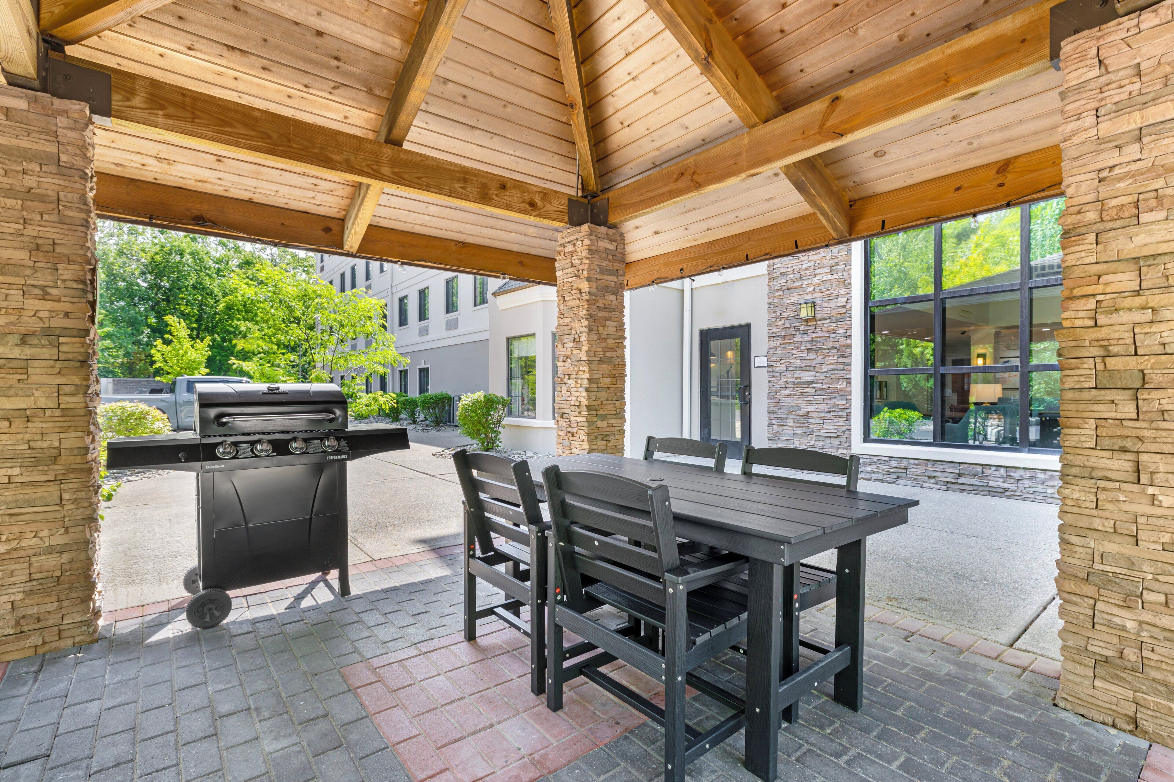 Een overdekt terras buiten, met een barbecue, een tafel en stoelen.
