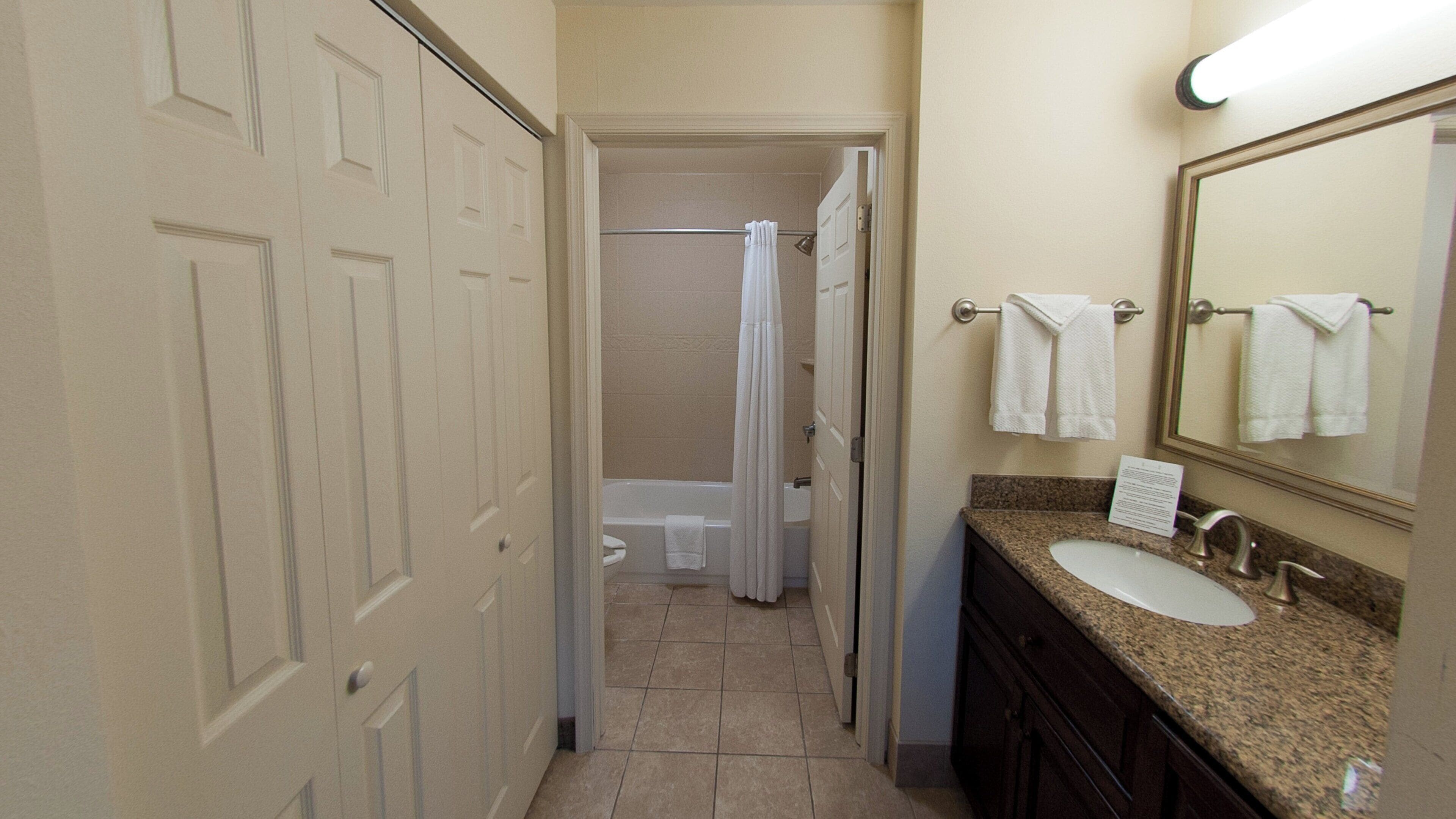 A hotel bathroom with a shower, toilet, sink, and towel rack.