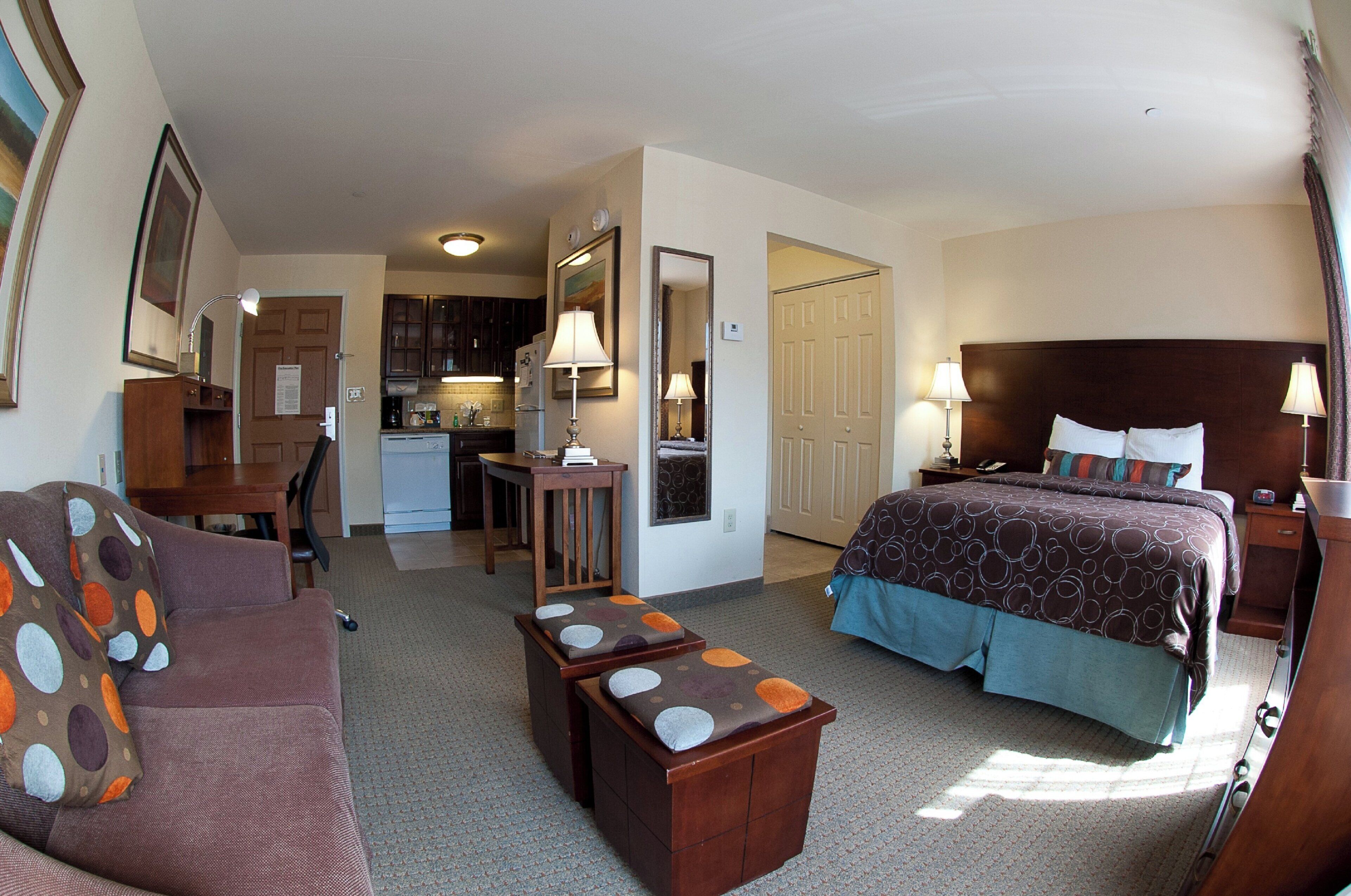 Habitación de hotel con cama, sofá, escritorio, silla, kitchenette y baño.