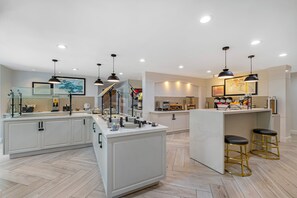 Une cuisine spacieuse avec des meubles blancs, un îlot central, des luminaires suspendus et un coin bar avec des tabourets.