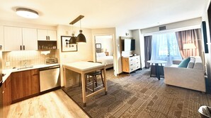 A compact hotel room with a kitchenette, a dining area, a sofa, and a TV.