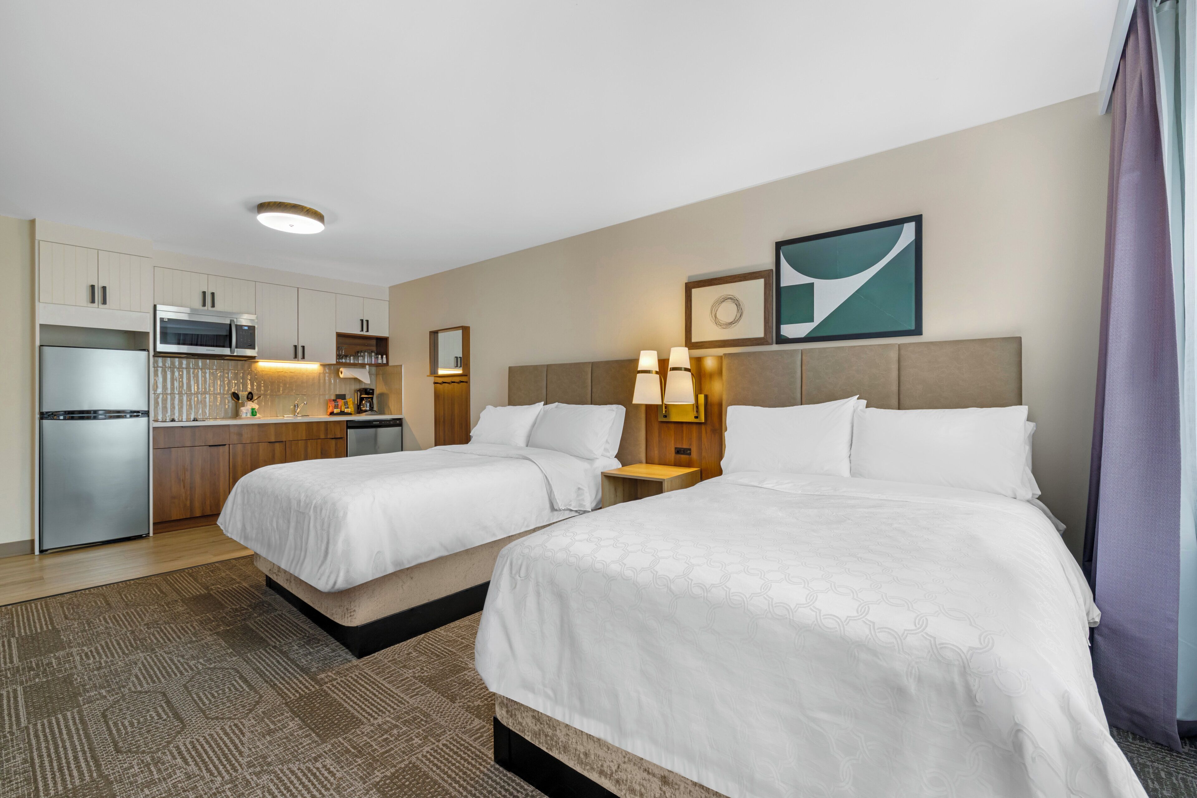 Ein Hotelzimmer mit zwei Betten, einer Küchenzeile, einem Badezimmer und Blick auf die Stadt.