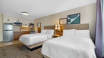 Ein Hotelzimmer mit zwei Betten, einer Küchenzeile, einem Badezimmer und Blick auf die Stadt.