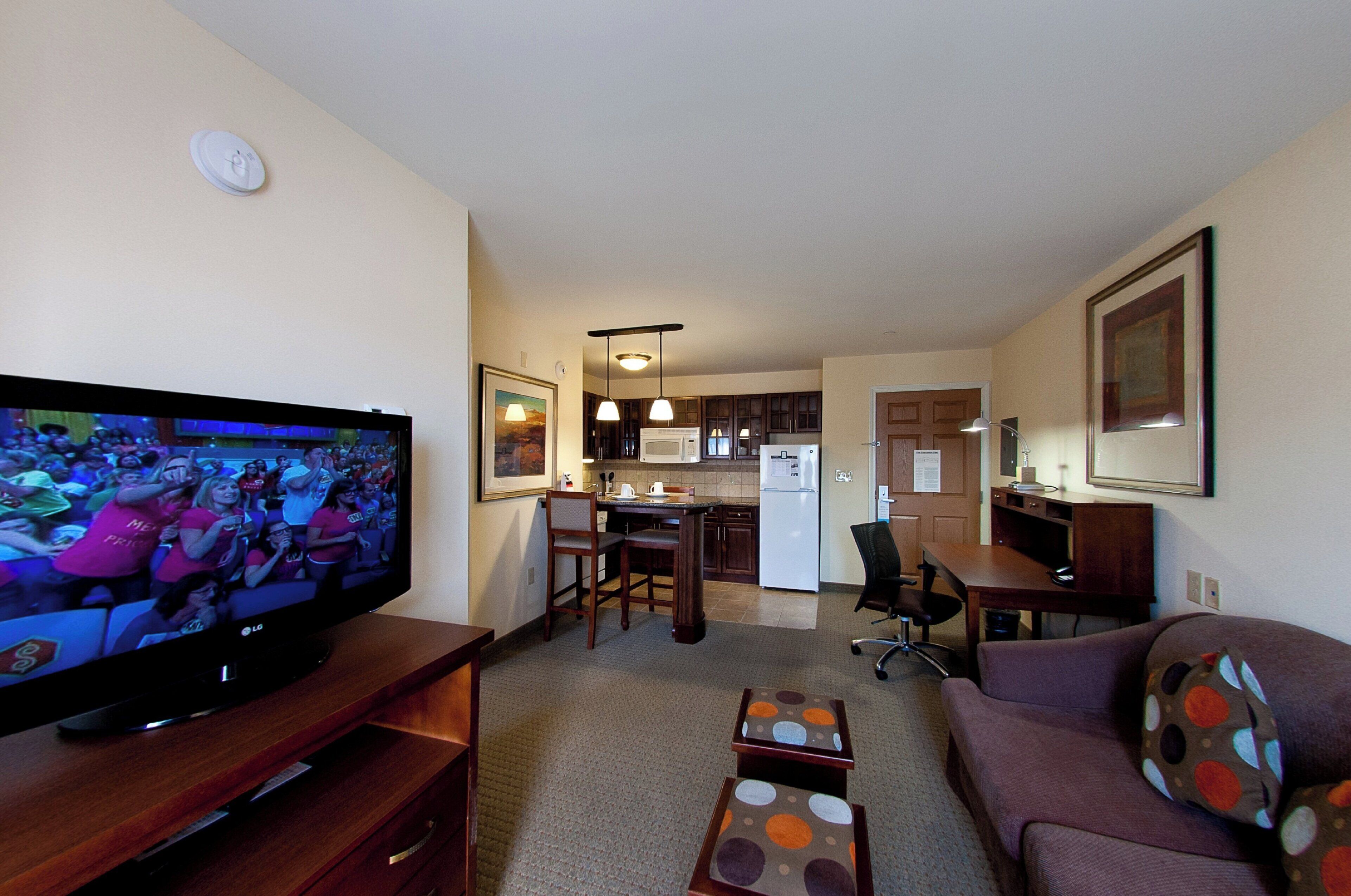 Una sala de estar con una televisión de pantalla plana, un sofá, una mesa de centro y una cocina al fondo.